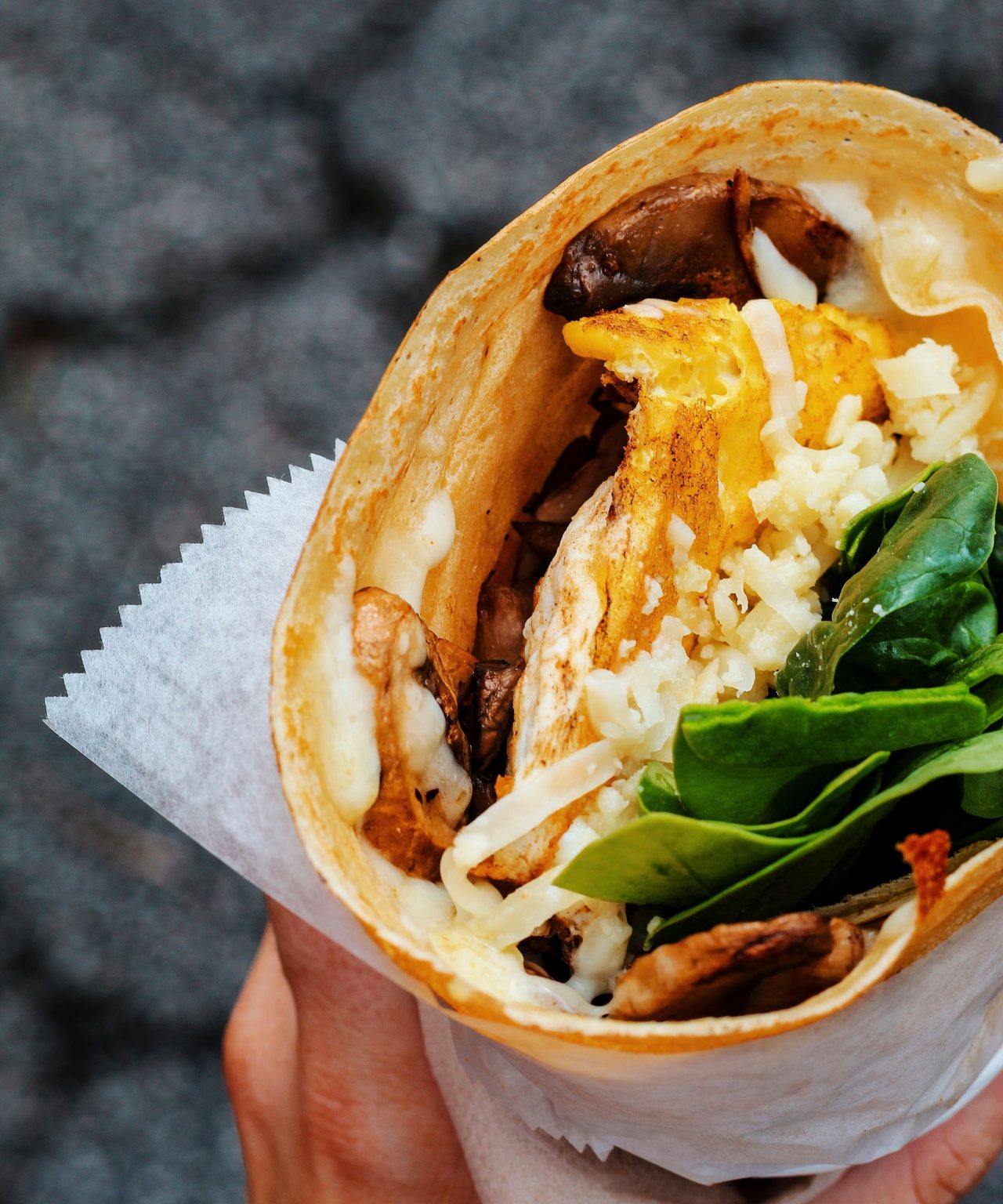 Galette pliée façon street food, garnie et tenue à la main dans son papier