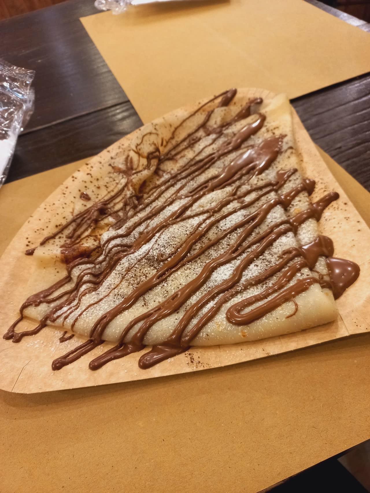 Crêpe nappée de chocolat servie sur papier, style street food